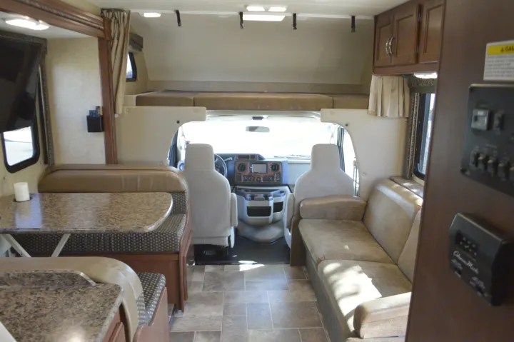 Inside this rv rental, find a cozy dinette, sofa, overhead bunk, and cockpit area, ideal for comfortable travel.. Thor Motor Coach Chateau 29G 2016