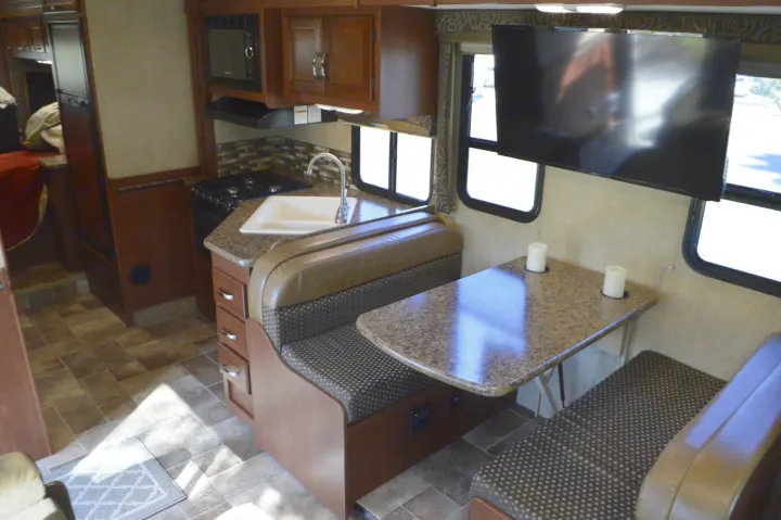 Spacious RV rental interior features a functional kitchen, comfortable dinette booth, and a wall-mounted TV.. Thor Motor Coach Chateau 29G 2016