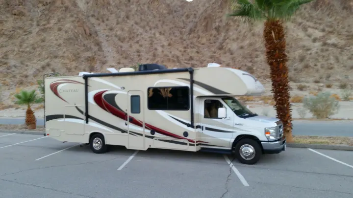 Light-colored Class C rv rental, a Chateau model, parked in a desert parking lot with palm trees.. Thor Motor Coach Chateau 29G 2016