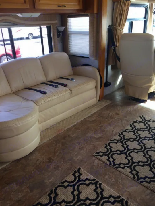 Spacious RV rental interior featuring a cream leather sofa with seatbelts, a matching recliner, and stylish patterned rugs on the floor.. Fleetwood Discovery 2005