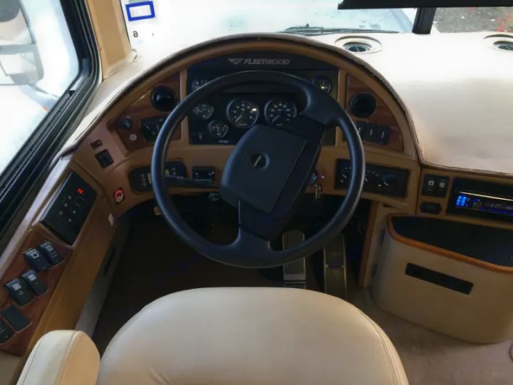 The driver's cockpit of a Fleetwood RV, showing the steering wheel, dashboard, and controls. Ideal for an RV rental trip.. Fleetwood Discovery 2005