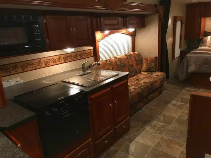 RV rental interior showcasing a kitchenette, sofa, and bed area. Brown cabinets and tiled floors create a warm, functional space.. Forest River Wildwood 2011