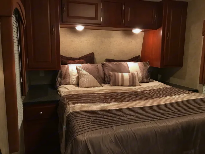 Cozy RV rental bedroom with a large bed, overhead cabinets, and reading lights. Ideal for a comfortable road trip.. Forest River Wildwood 2011