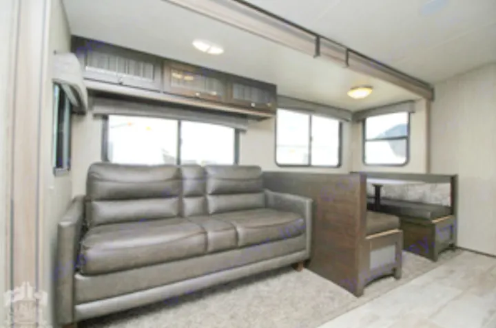 Dark brown sofa and dining booth inside this well-lit RV rental living area with multiple windows and overhead cabinets.. Heartland Sundance 2019