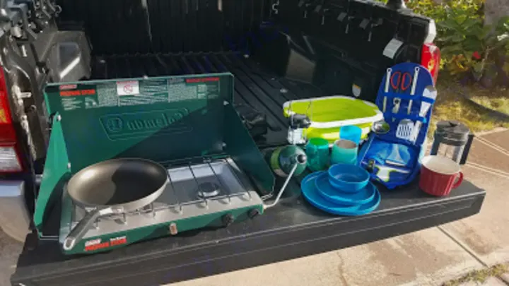 Setup for an RV rental adventure: Coleman stove, pan, dishes, and kitchen tools displayed on a truck tailgate.. toyota tacoma 2023