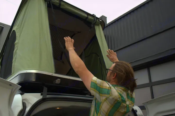 Man setting up a roof-top tent on an RV rental vehicle, reaching into the open green tent.. Ram Promaster City 2018