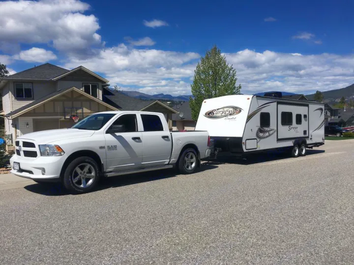 White truck towing a white travel trailer on a sunny street. Your next RV rental adventure awaits!. Forest River Surveyor 2014