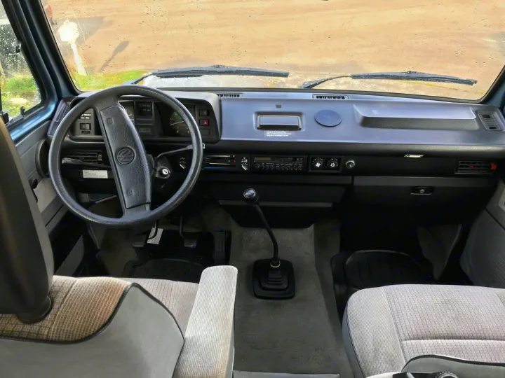 Interior of a classic RV rental, showing the dashboard, steering wheel, manual shifter, and front seats. Perfect for a road trip!. Volkswagen Westfalia 1989