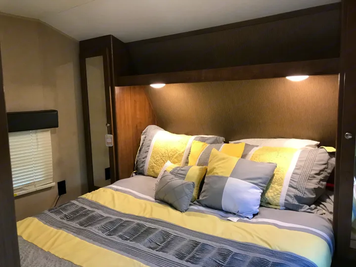 A modern RV rental bedroom features yellow and grey bedding, bright overhead lights, and efficient built-in storage solutions.. Dutchmen Aspen Trail 2018