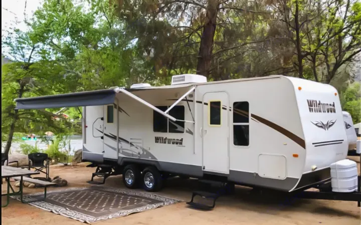 This RV rental, a Wildwood travel trailer, is set up riverside with an awning, outdoor rug, and picnic table.. Forest River Wildwood 2011