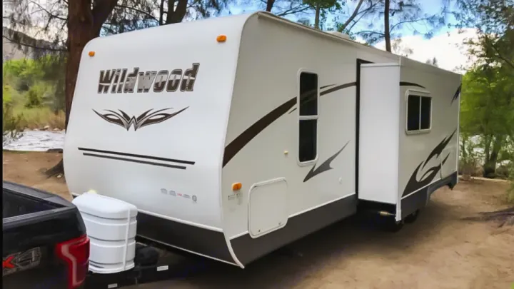 White Wildwood travel trailer RV rental with slide-out, parked at a scenic campground and hooked to a pickup truck.. Forest River Wildwood 2011