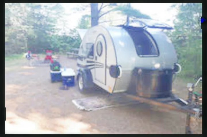 Compact travel trailer RV rental is set up at a sandy, treed campsite with coolers for camping.. Little Guy Silver Shadow 2016