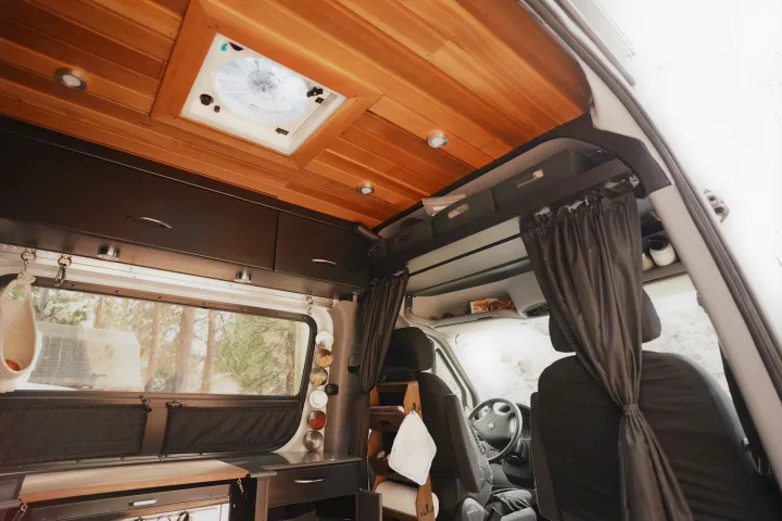 Inside a modern rv rental van: wood ceiling, recessed lights, custom storage, and front cab with privacy curtains, designed for comfort.. Freightliner Sprinter 2016