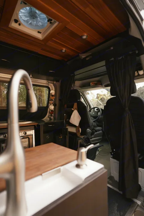 Inside an RV rental van: a well-equipped kitchen with sink & oven, wood ceiling, and front cabin with a driver. Adventure awaits!. Freightliner Sprinter 2016