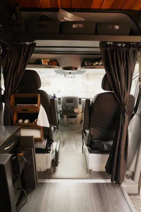 Cozy RV rental interior looking towards the front cabin, featuring organized storage, privacy curtains, and custom shelving.. Freightliner Sprinter 2016