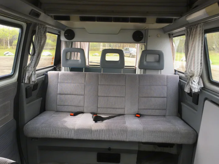 Inside an RV rental: Rear bench seat with three headrests, side/rear windows with curtains, and speakers for comfortable travel.. Volkswagen Weekender 1991