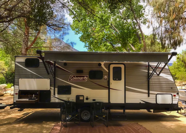 This Coleman RV rental, equipped with an outdoor kitchen and awning, sits under shady trees with mountains in the background.. Coleman Lantern 2018