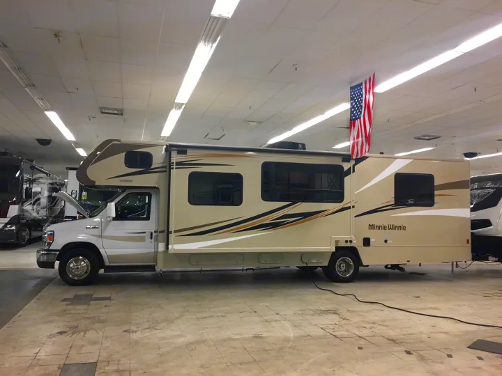 Side view of a beige/white Minnie Winnie motorhome displayed indoors, ideal for an RV rental.. Winnebago Minnie Winnie 2017