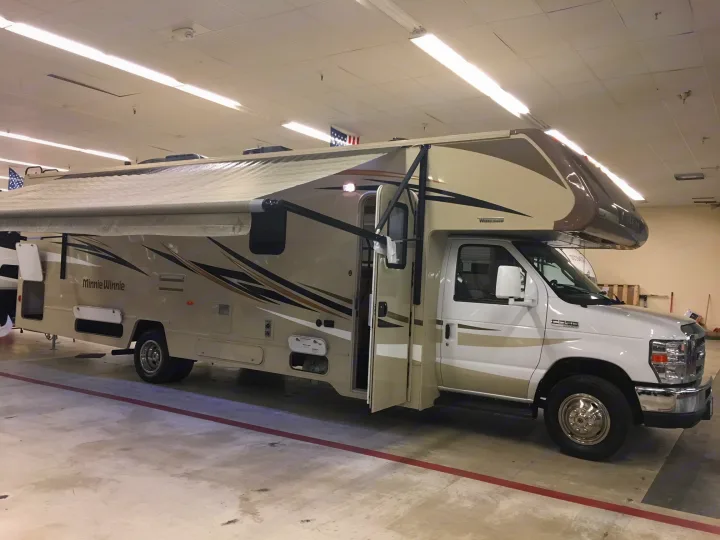Minnie Winnie RV rental, a tan & white motorhome with awning extended, parked indoors. Ready for your next adventure.. Winnebago Minnie Winnie 2017