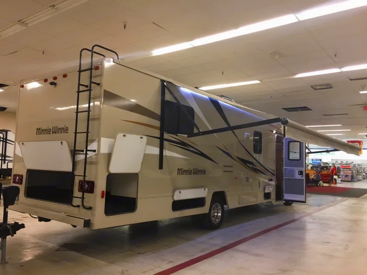 A beige Minnie Winnie RV, with open compartments and an extended awning, is displayed indoors, likely for rv rental or sale.. Winnebago Minnie Winnie 2017