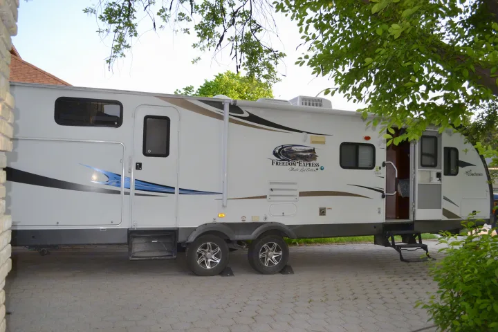 A white Coachmen Freedom Express rv rental, complete with steps and decals, is parked on pavers with trees overhead.. Coachmen Freedom Express 2013