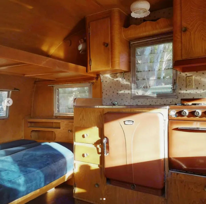 Inside a classic rv rental: warm wood, compact kitchen with a retro fridge, and a blue mattress bed. Ready for adventure!. Shasta Oasis 1959