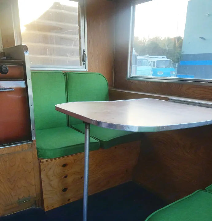 This RV rental interior features a wooden dining area with bright green cushions, and a large window view.. Shasta Oasis 1959