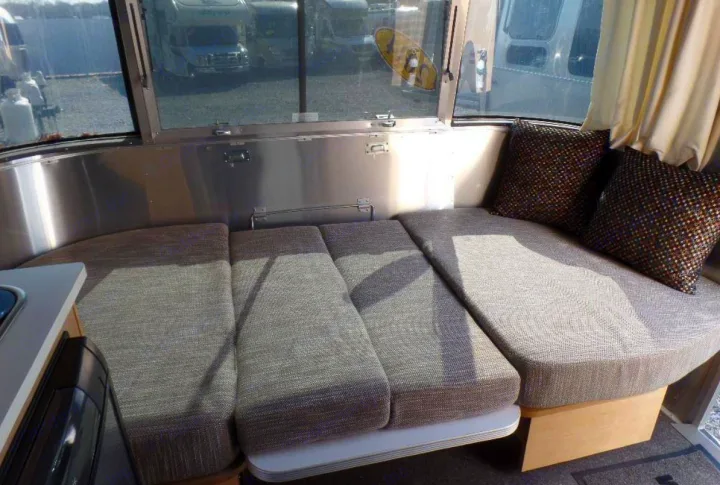 RV rental interior: Curved dinette lounge with grey fabric cushions, metallic walls, & window view of other RVs.. Airstream Sport 2015