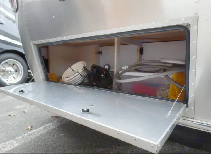 Airstream RV rental exterior storage compartment open, revealing coiled hoses, clear bin with items, and organized space.. Airstream Sport 2015