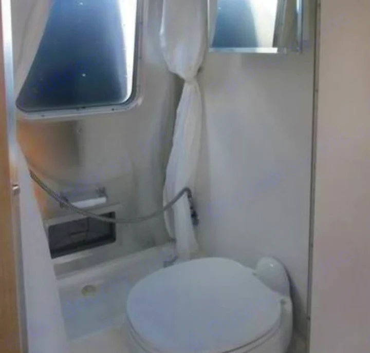 RV rental compact bathroom with toilet, handheld shower, and window. Efficient design for travel comfort.. Airstream Sport 2015