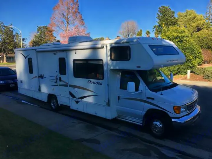 White Class C Winnebago Outlook RV rental parked curbside. This motorhome is ready for your next road trip adventure.. Winnebago Outlook 2006