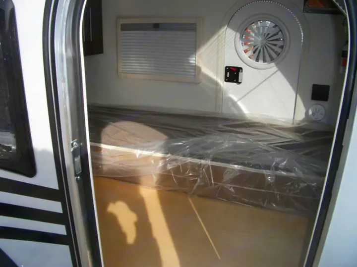Interior view of a new rv rental camper, showing the bed wrapped in plastic, window, and vent. Ready for travel!. Little Guy Silver Shadow 2016
