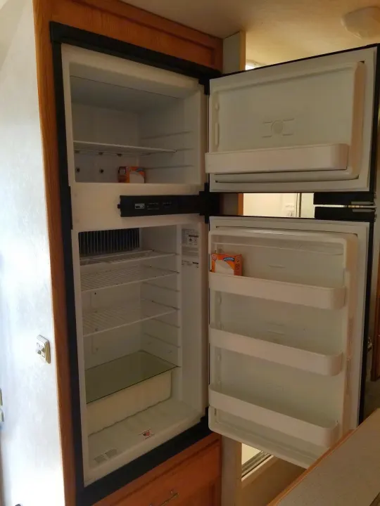 Inside a clean, empty RV rental refrigerator with doors open, showing its top freezer and main compartment.. Winnebago Outlook 2006