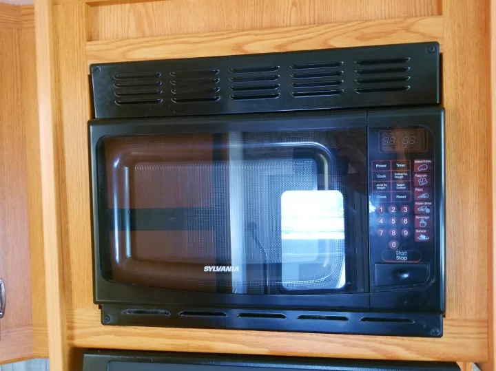 Black Sylvania microwave oven in an rv rental kitchen, featuring a visible control panel and glass door.. Winnebago Outlook 2006