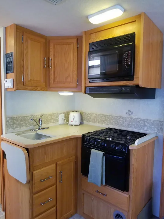 Functional RV rental kitchen: wood cabinets, sink, microwave, stove, and handy pull-out counter space.. Winnebago Outlook 2006