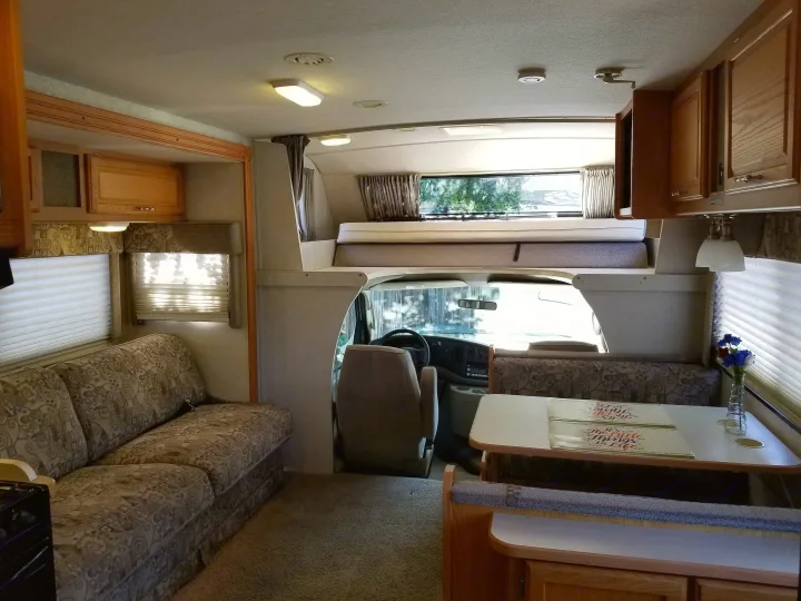 Cozy rv rental living area featuring a plush sofa, inviting dinette, and overhead bed. Comfort awaits your road trip.. Winnebago Outlook 2006