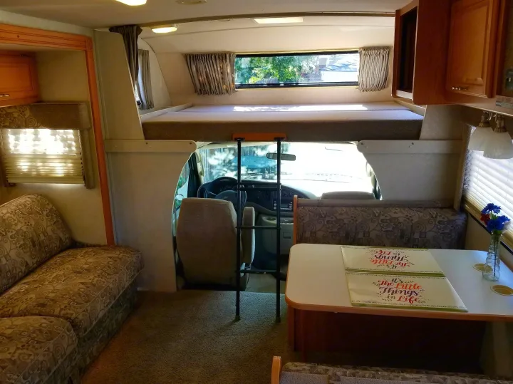 Cozy RV rental interior with a dinette, sofa, and over-cab sleeping area for comfortable travel.. Winnebago Outlook 2006
