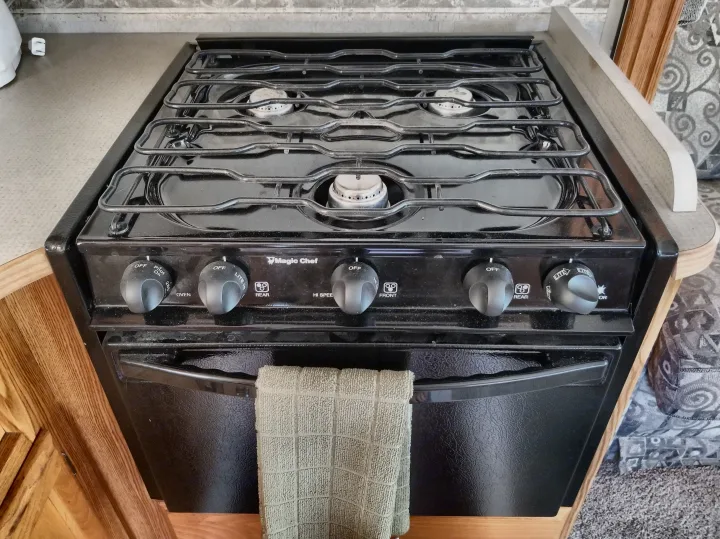 An RV rental kitchen showcasing a black Magic Chef gas stove with four burners, an oven, and a hanging towel. Perfect for cooking.. Winnebago Outlook 2006