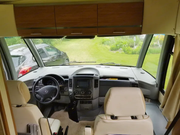 Inside a spacious Mercedes-Benz **RV rental**, showing the cockpit area and a serene outdoor view from the windshield.. Itasca Reyo 2014