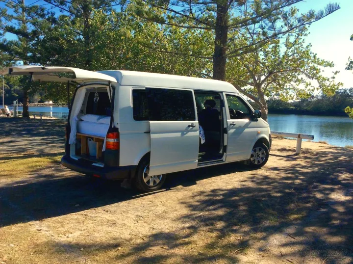 White RV rental campervan by tranquil waters, rear open showing its cozy bed. Perfect for travel & van life.. Volkswagen Transporter T5 2005