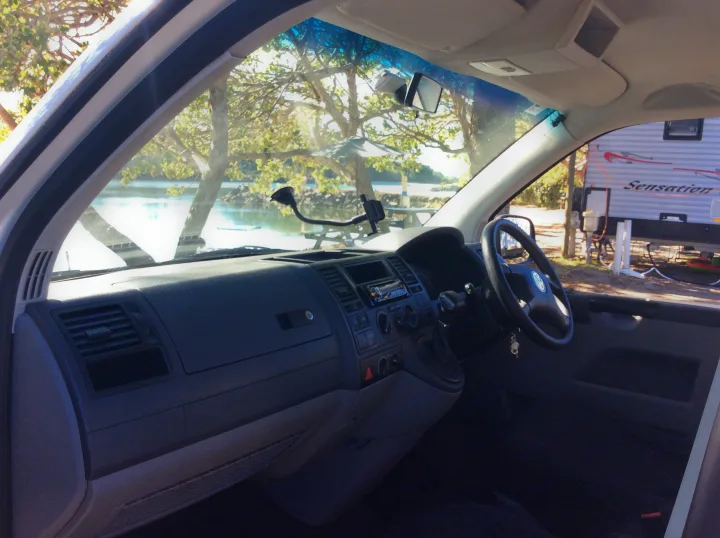 Inside an RV rental, showing the dashboard and steering wheel, with a view of a scenic campsite, water, and another RV outside.. Volkswagen Transporter T5 2005