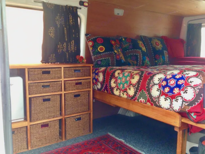 Cozy RV rental interior featuring a vibrant bed, practical basket storage, and mini-fridge. Ideal for comfortable van life adventures.. Mercedes-Benz Sprinter 2005