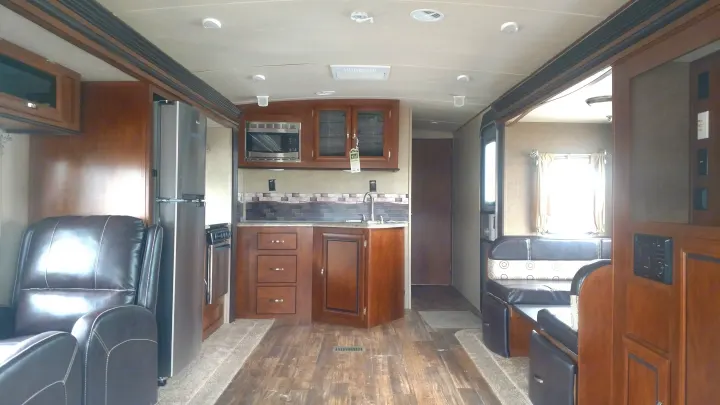 Spacious RV rental interior: view of a kitchen with stainless appliances, dining booth, and comfortable recliner.. Forest River Vibe 2016