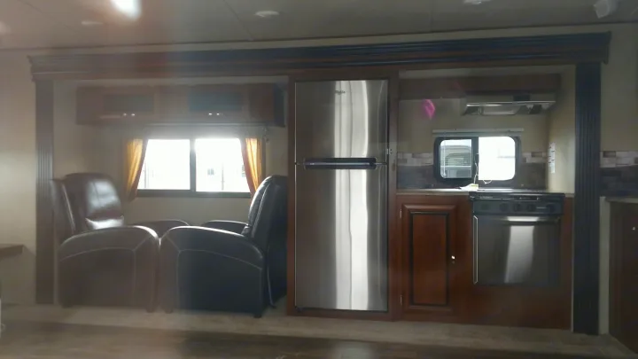 Explore this RV rental's cozy interior, featuring comfortable recliners, a stainless steel fridge, and a functional kitchen.. Forest River Vibe 2016