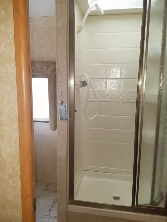 Clean rv rental shower with white, tile-patterned walls, handheld showerhead, textured glass door. Protective floor visible.. Four Winds Chateau Sport 2008