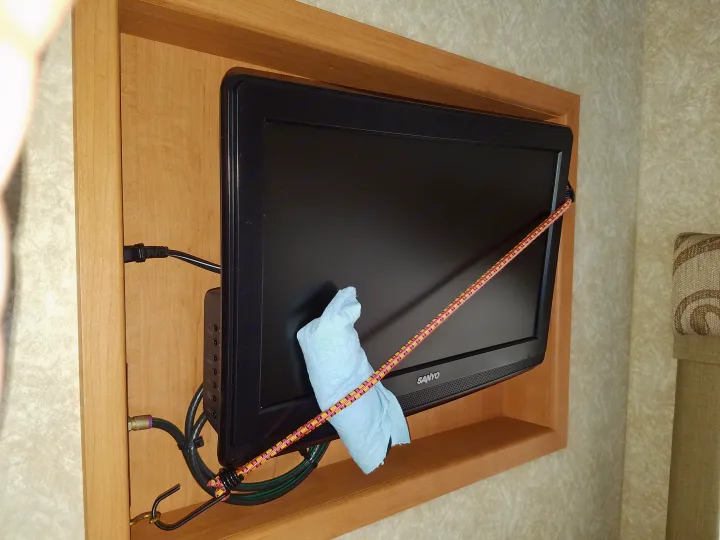 RV rental: A Sanyo TV is secured in a wooden recess with a bungee cord and a light blue cloth, ready for travel. Cables visible.. Four Winds Chateau Sport 2008
