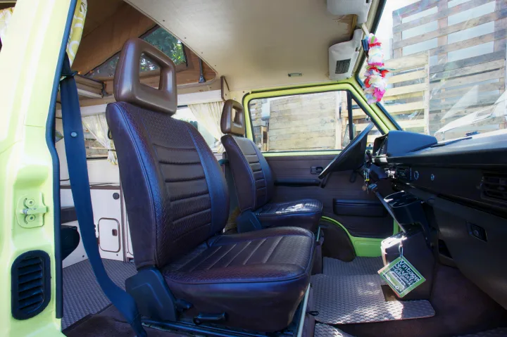 Inside a lime green RV rental camper van, featuring brown patterned seats, dashboard, and rear camper conversion with pop-top.. Volkswagen westfalia 1984