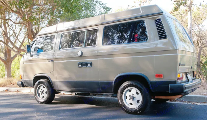 Classic beige VW Vanagon camper van, ideal for your next rv rental adventure, parked on asphalt with trees.. Volkswagen Westfalia 1986
