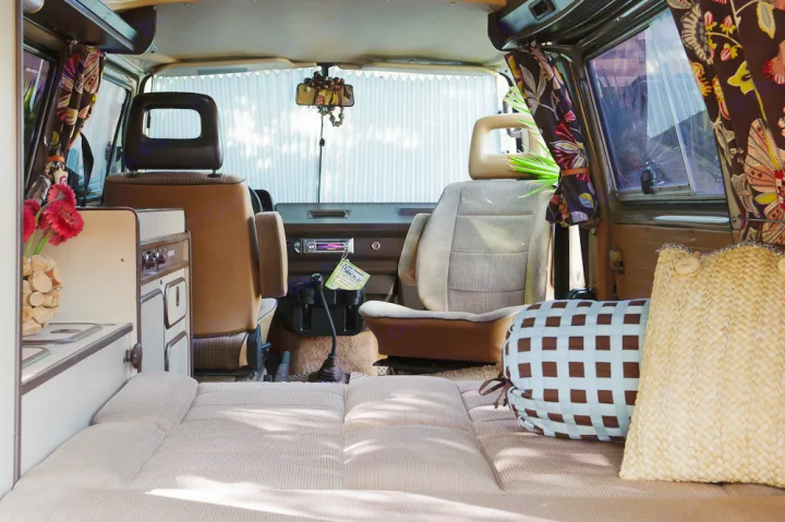 Cozy RV rental interior: view from bed to front seats, showing kitchenette, sunlit cabin, and patterned curtains.. Volkswagen Westfalia 1986