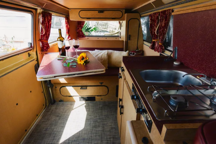Step inside this cozy RV rental's inviting interior! Features a dining area with wine, a flower, and a compact kitchen.. Volkswagen Westfalia 1978